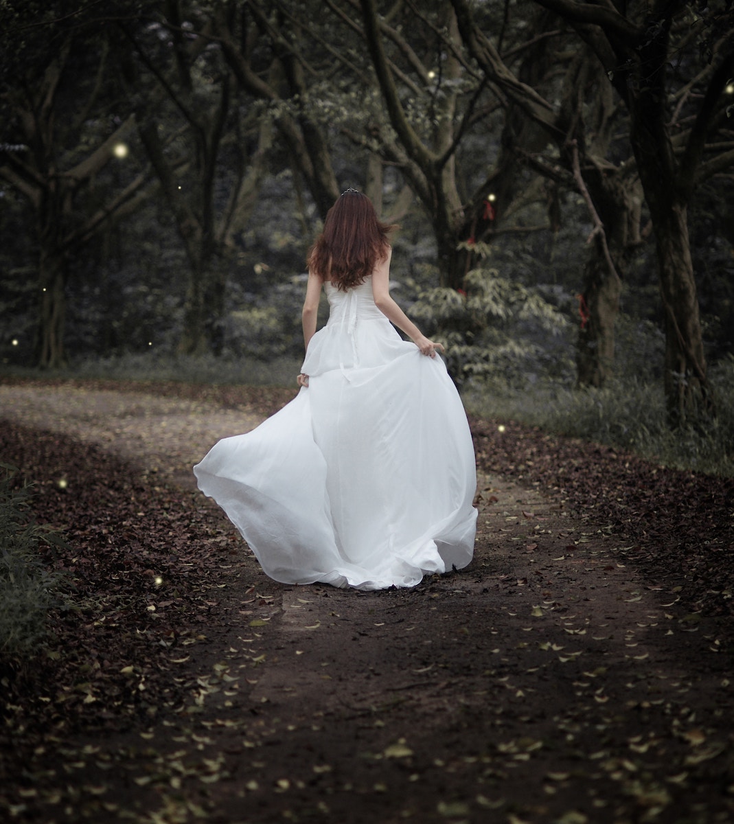 woman in fancy white dress running away on forest path, with sparkles in the air